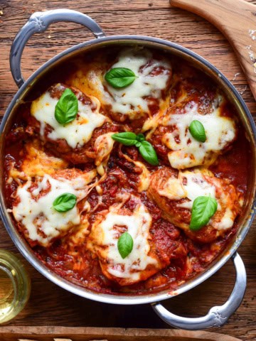 Tomato braised chicken parm thighs topped with melted cheese and fresh basil.