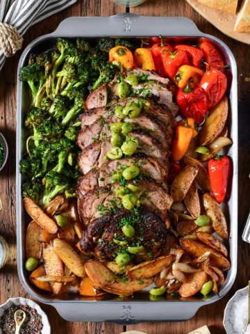 A sliced slow roasted pork butt with crushed olives and parsley. Served on a sheet pan with roasted fingerling potatoes, peppers and broccoli.