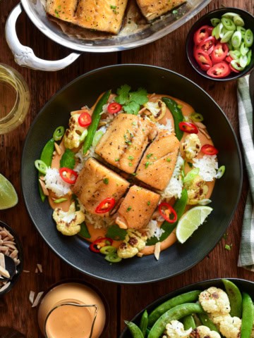 Baked black cod served in a bowl with Thai peanut curry sauce, crispy rice, roasted cauliflower, snap peas, red chilli peppers and a lemon wedge.