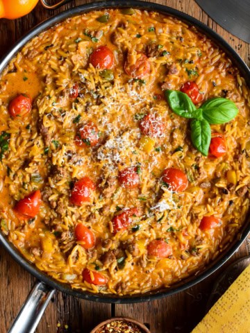 A creamy sausage, pepper & tomato orzo skillet topped with shaved Parmesan and fresh basil.