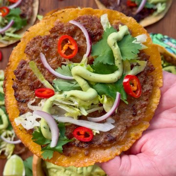 A close-up of crispy pork smash tacos with avocado lime cream, cilantro, onions, lettuce and chiles.
