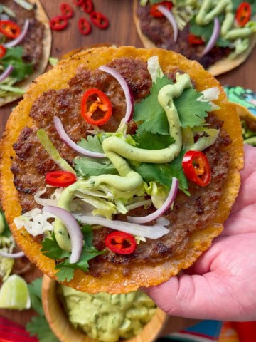 A close-up of crispy pork smash tacos with avocado lime cream, cilantro, onions, lettuce and chiles.