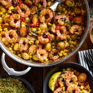 A skillet of spicy Calabrian shrimp with corn and potatoes. Served in a bowl with a lemon pangrattato sprinkled over it.