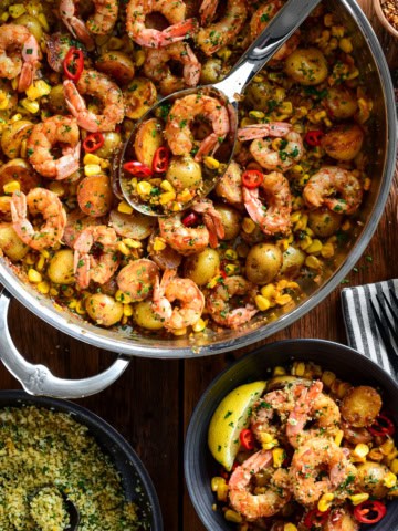 A skillet of spicy Calabrian shrimp with corn and potatoes. Served in a bowl with a lemon pangrattato sprinkled over it.