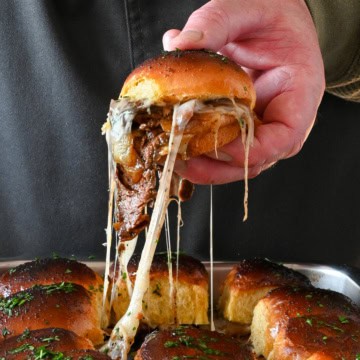 A steak fajita slider is getting lifted out of a pan of sliders with a cheese pull.