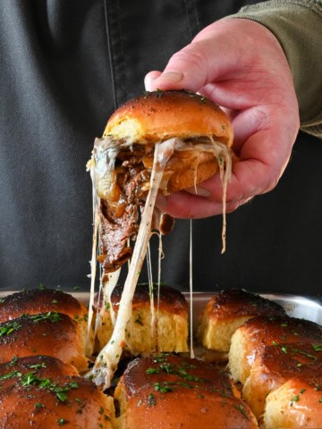 A steak fajita slider is getting lifted out of a pan of sliders with a cheese pull.