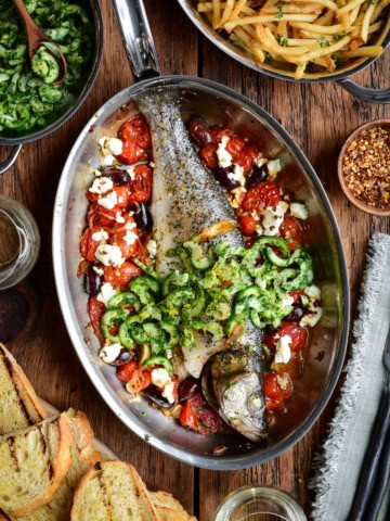 A whole roasted branzino in a fish pan with tomatoes, feta and olives. Served with toasted sourdough, a cucumber slaw and shoestring fries.