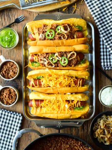 A tray with four chili cheese dogs, two have no chili. The chili is served in small cups to pour over the dogs.
