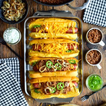 A tray with four chili cheese dogs, two have no chili. The chili is served in small cups to pour over the dogs.