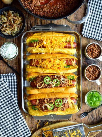 A tray with four chili cheese dogs, two have no chili. The chili is served in small cups to pour over the dogs.