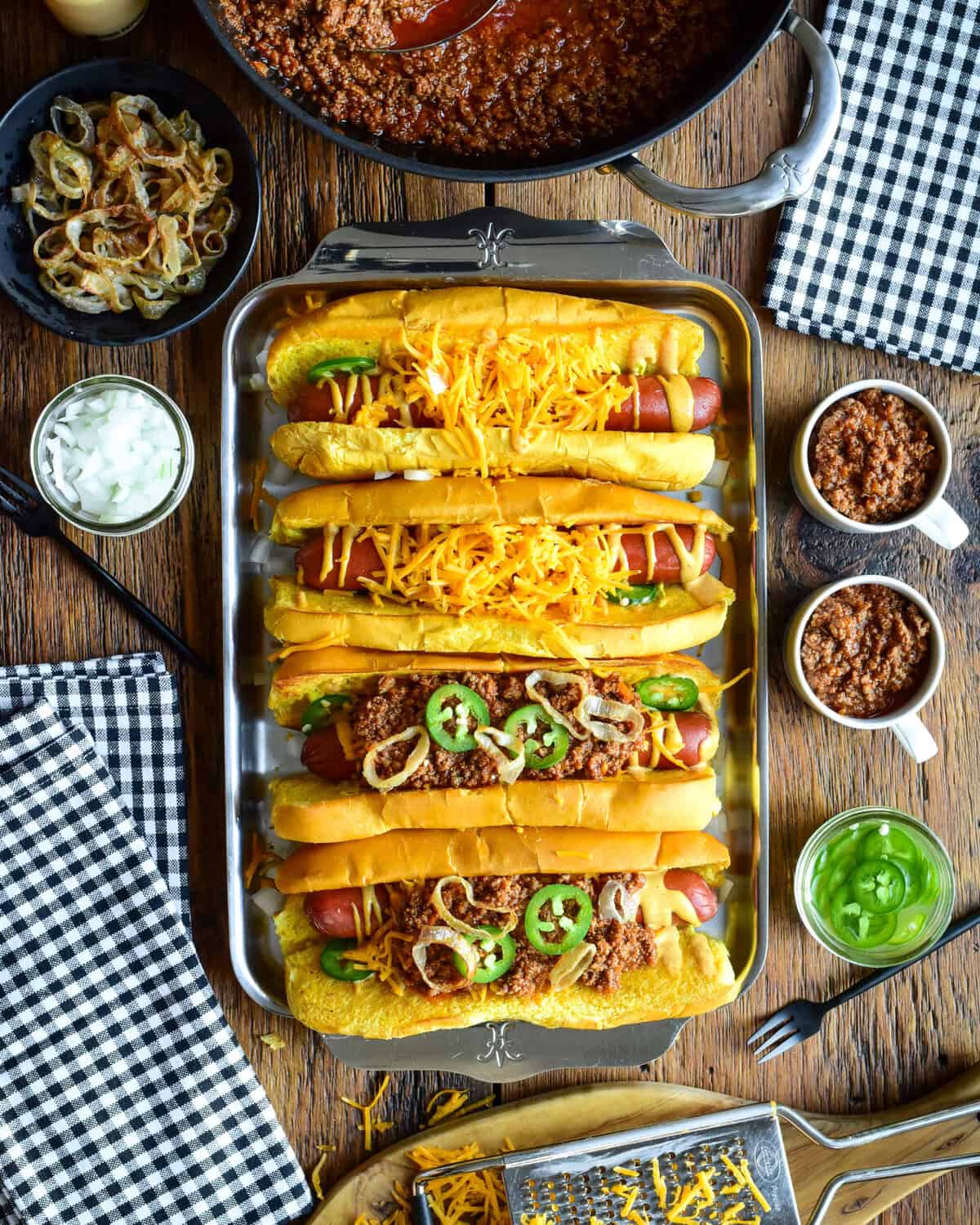 A tray with four chili cheese dogs, two have no chili. The chili is served in small cups to pour over the dogs.