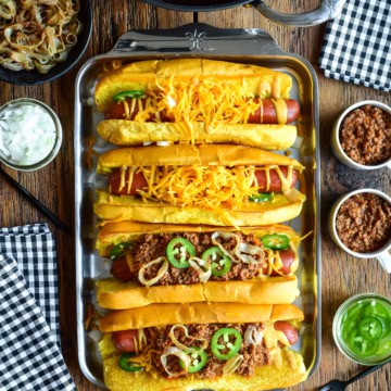 A tray with four chili cheese dogs, two have no chili. The chili is served in small cups to pour over the dogs.