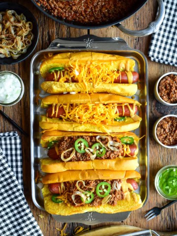 A tray with four chili cheese dogs, two have no chili. The chili is served in small cups to pour over the dogs.
