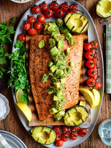 Cedar plank salmon topped with a smoky, chunky grilled avocado chimichurri salsa and charred tomatoes on the vine.
