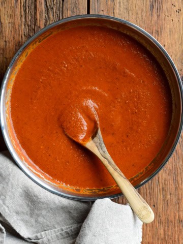 A skillet of homemade fire-roasted enchilada sauce with a wooden spoon.