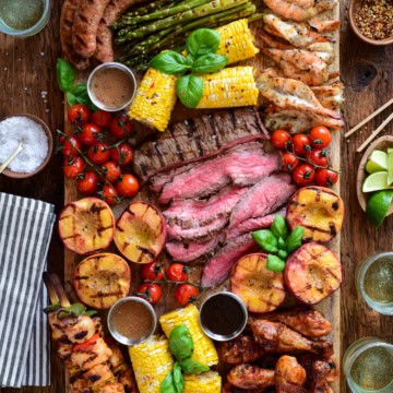 Colorful grilled meats, vegetables, and sides on a wooden board for a BBQ charcuterie platter.