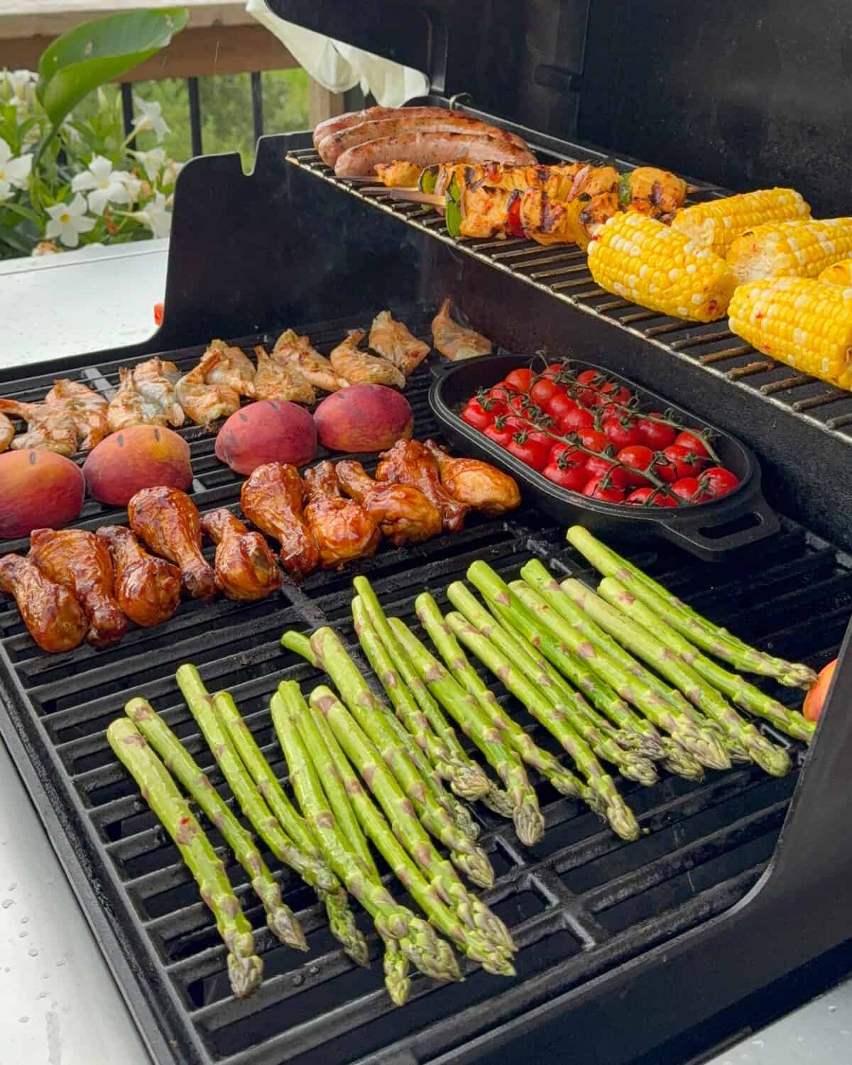A full grill with two rack filled with chicken wings, skewers, sausages, shrimp, peaches, tomatoes and corn.