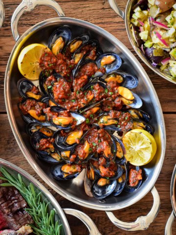 Mejillones en Salsa Picante Spanish Mussels on Half Shell served in an oval au gratin with grilled lemon wedges.