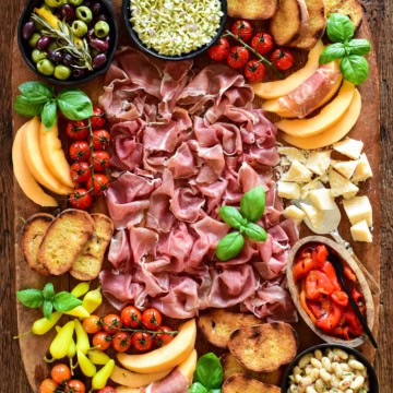 A Prosciutto di Parma Antipasto Butter Board with whipped butter, marinated white beans, melon, marinated olives, tomatoes, grilled bread, parmesan cheese, pickled peppers and fresh basil.