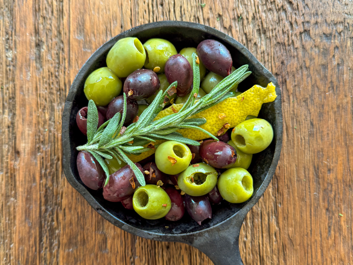 Mixed olives in a cast iron skillet marinated in olive oil, rosemary and lemon peel. The olives will get warmed up in this skillet.