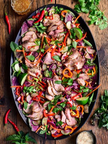 A colourful platter with a Spicy Thai Pork Tenderloin Crunchy Herb Salad. Served with a crispy roasted rice powder, extra herbs and dressing.