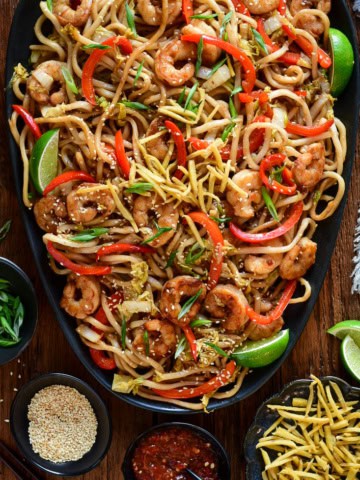 A platter of Sticky Soy Argentinian Shrimp & Fried Ginger Udon. Served with extra fried ginger, limes, sesame seeds and green onions.