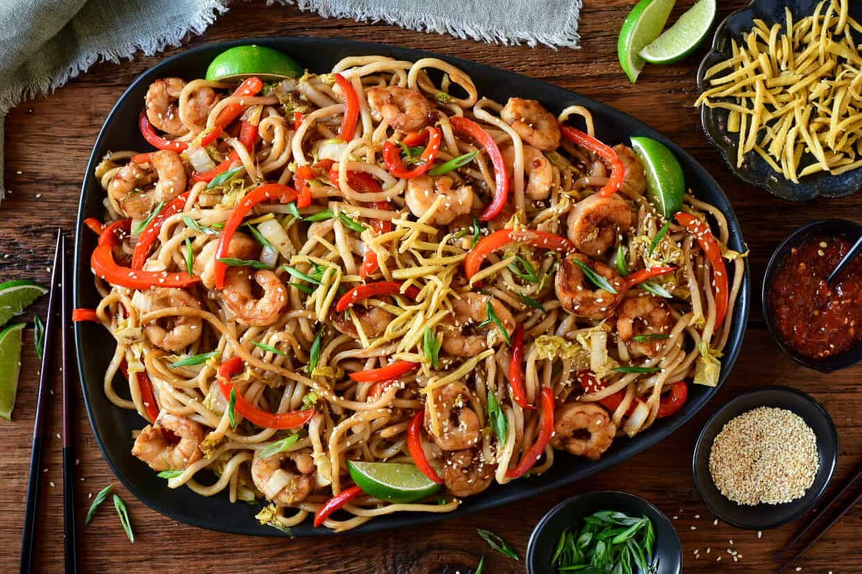 A platter of Sticky Soy Argentinian Shrimp & Fried Ginger Udon. Served with extra fried ginger, limes, sesame seeds and green onions.