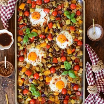 A stainless steel griddle with an Italian sausage and pepper breakfast hash with four fried eggs.