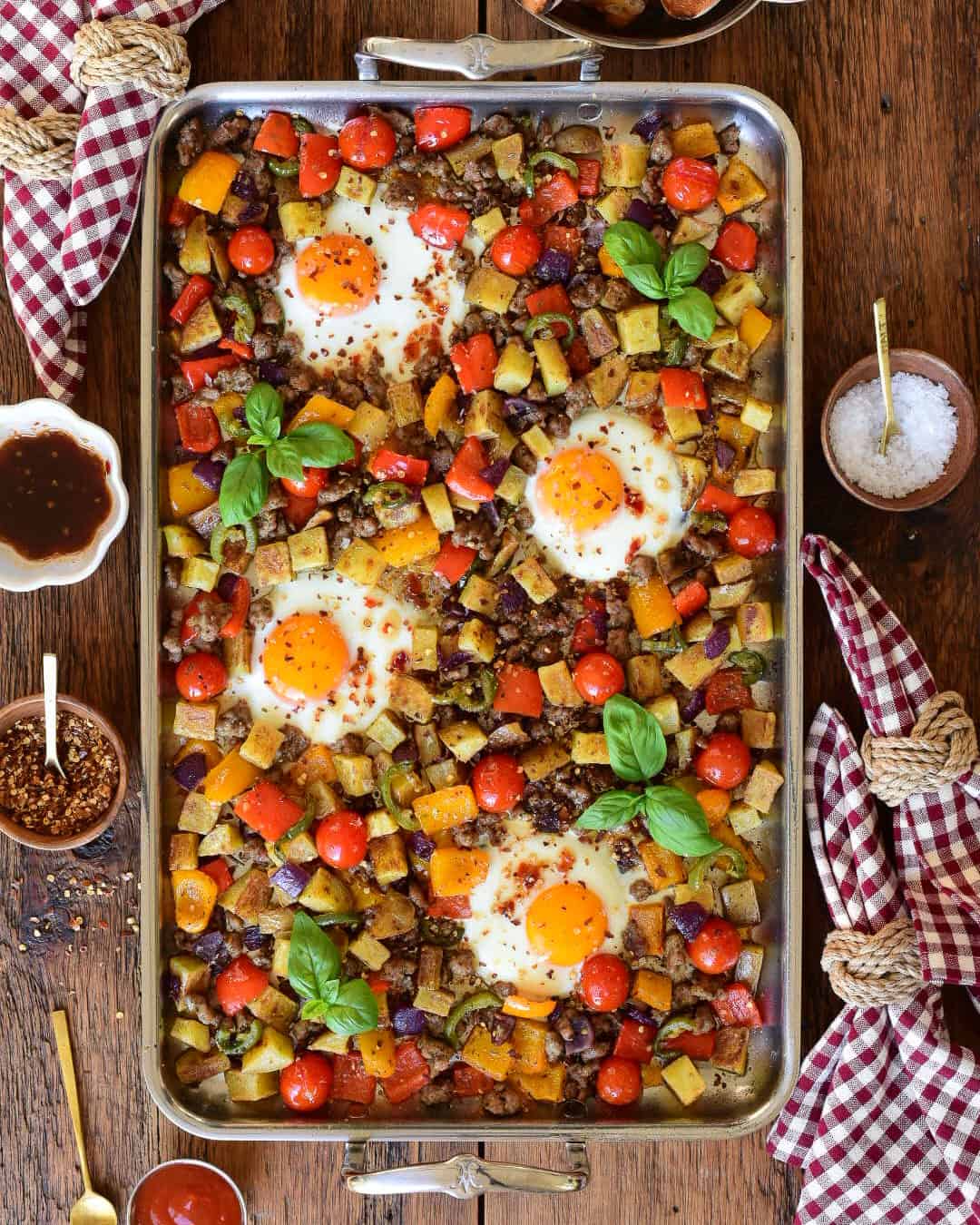 A stainless steel griddle with an Italian sausage and pepper breakfast hash with four fried eggs.