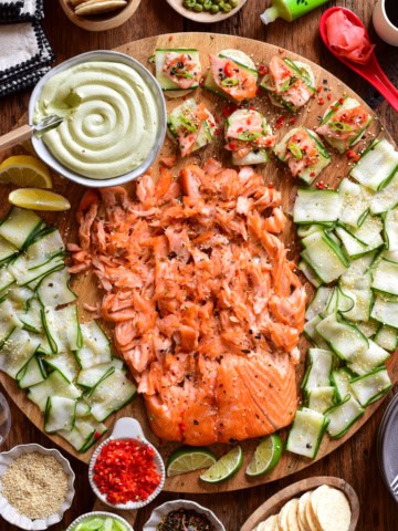 A Smoked Salmon Board with Avocado Lime Cream Cheese served on a round board with extra toppings surrounding it.